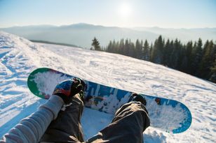 Un snowboardeur assis qui regarde sa planche et ses fixations