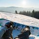 Un snowboardeur assis qui regarde sa planche et ses fixations