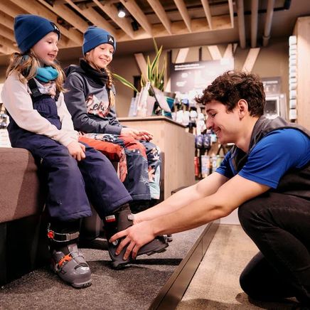 Un skiman ajuste la chaussure de ski à deux enfants souriants.