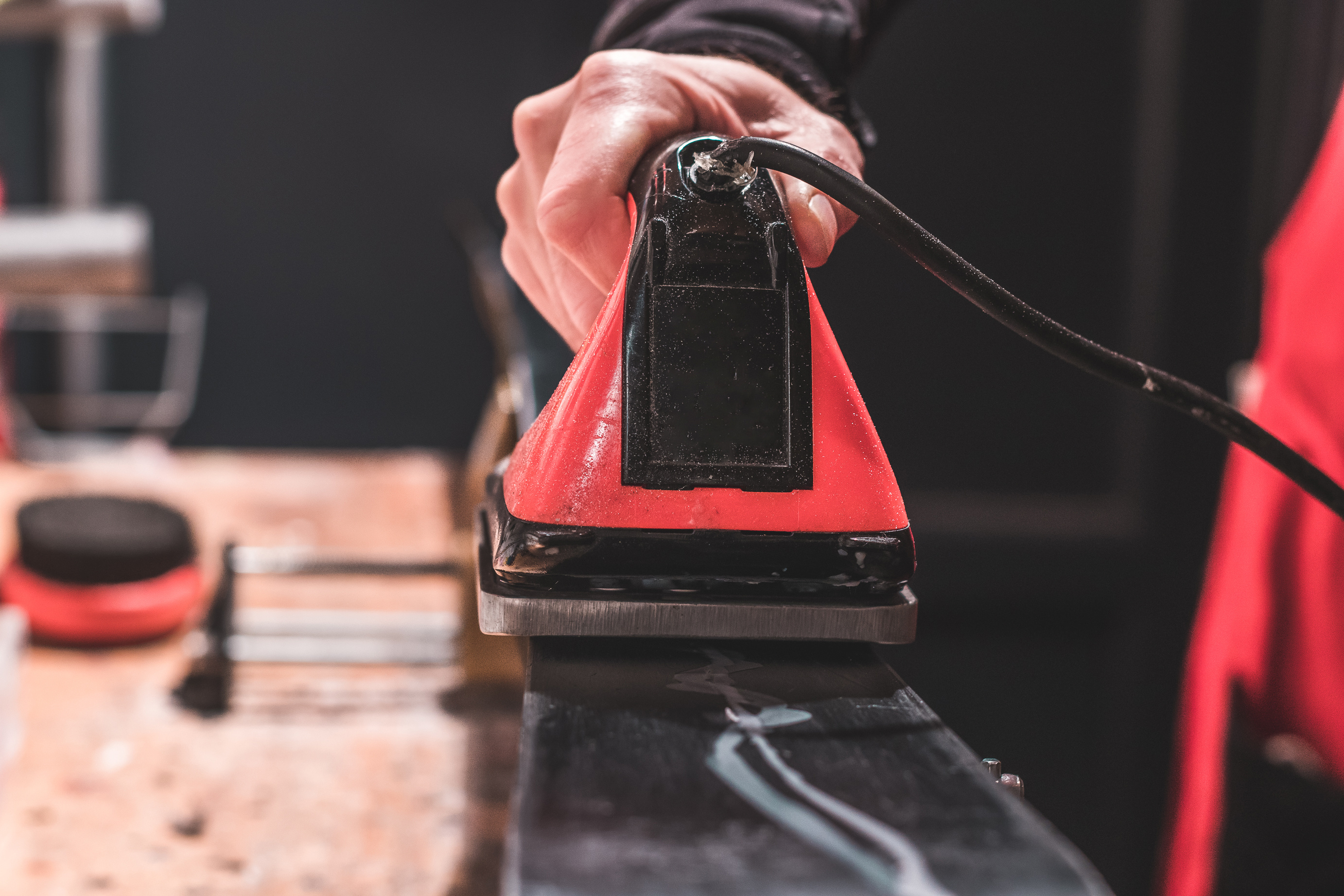Une main applique de la cire chaude sur un ski noir avec un fer à farter rouge.