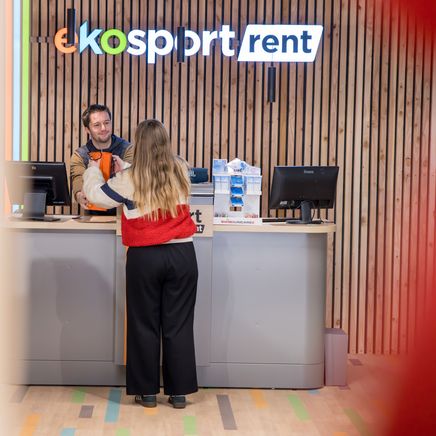 Un homme au comptoir remet un article à une femme devant un mur en lattes de bois avec l'enseigne "ekosport rent".
